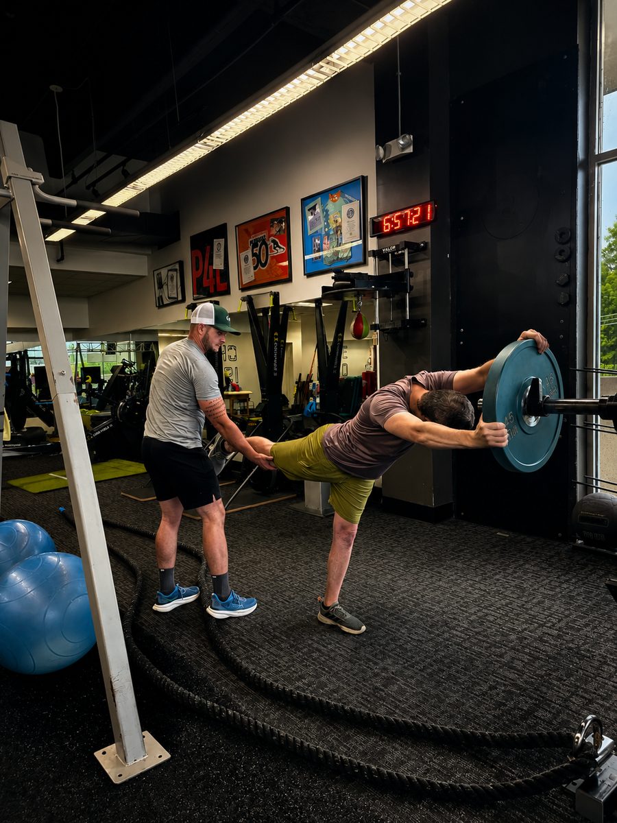 Brian spotting a client's single-leg deadlift with a barbell plate